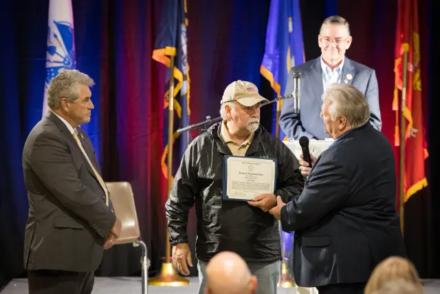 A man in a ball cap receives a certificate on stage