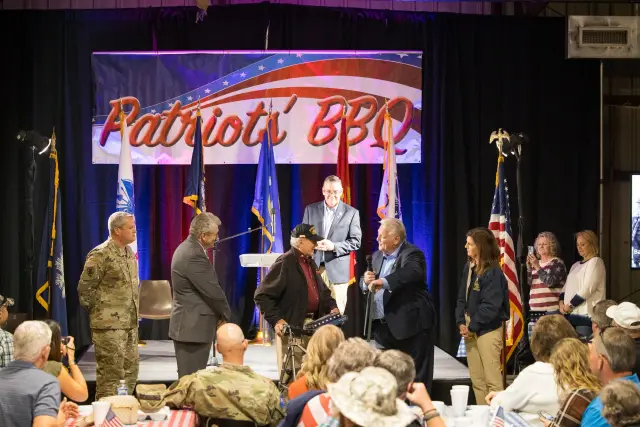 An older veteran is honored on stage as guests look on