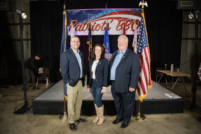 Three guests pose in front of the stage and flags